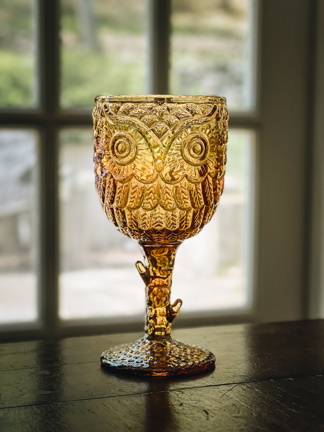 A green glass goblet embossed with an owl face design